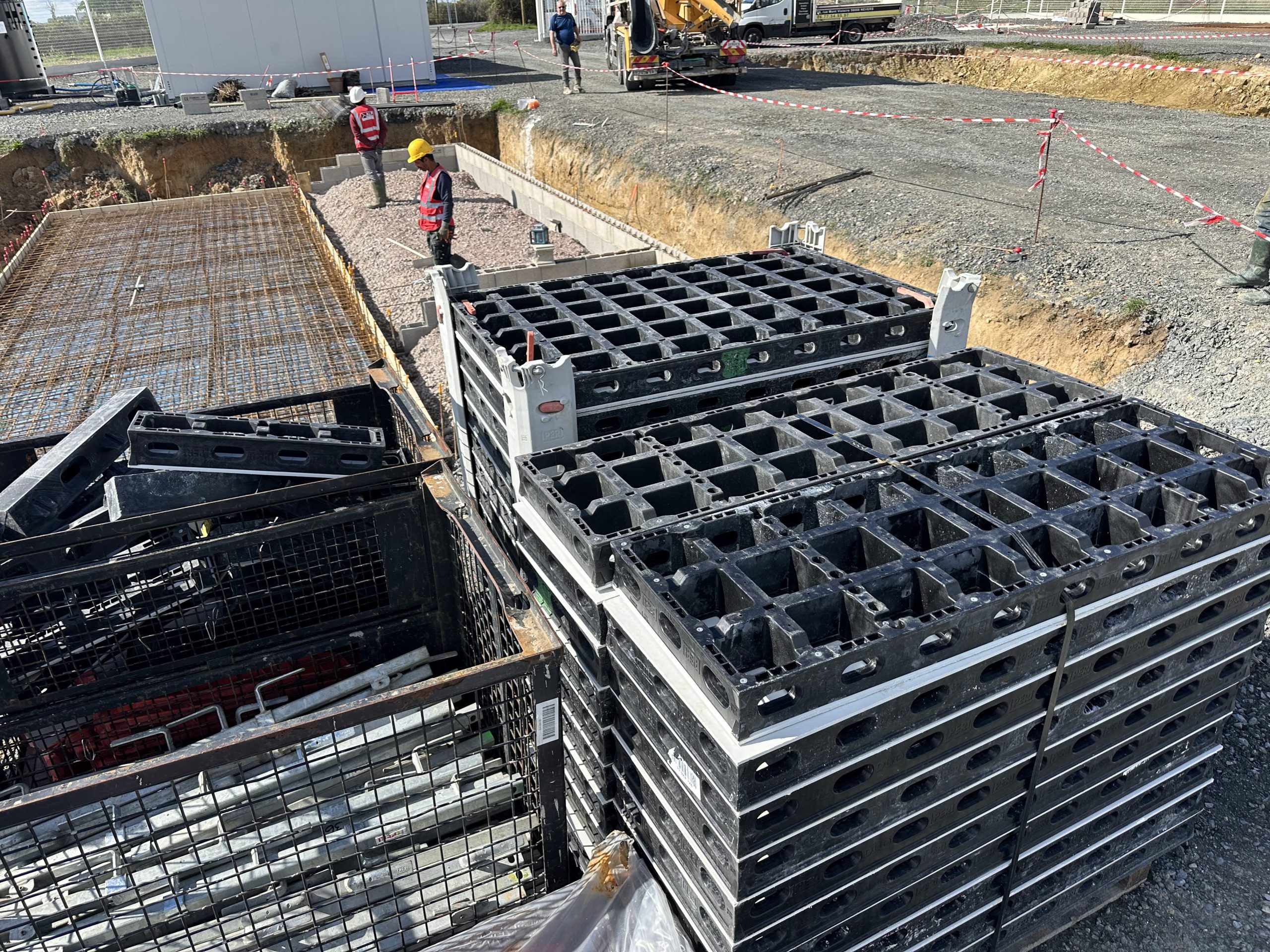 L&rsquo;&eacute;quipe pr&eacute;pare une dalle avec des treillis m&eacute;talliques et du coffrage, pr&egrave;s de panneaux de chantier empil&eacute;s.