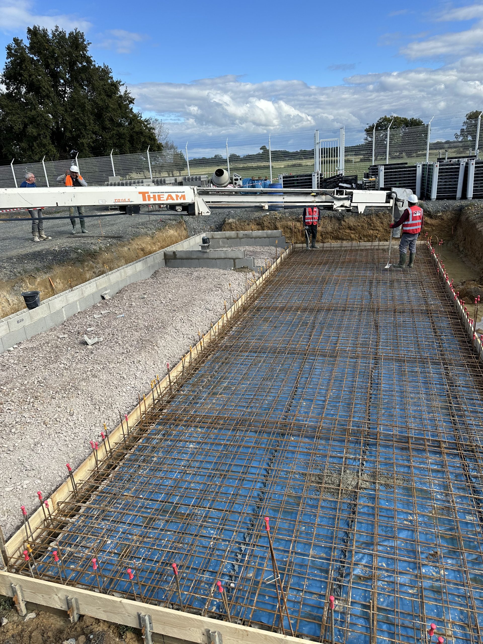 Une &eacute;quipe ALP r&eacute;alise le b&eacute;tonnage d&rsquo;une dalle avec une pompe, au-dessus du treillis m&eacute;tallique.