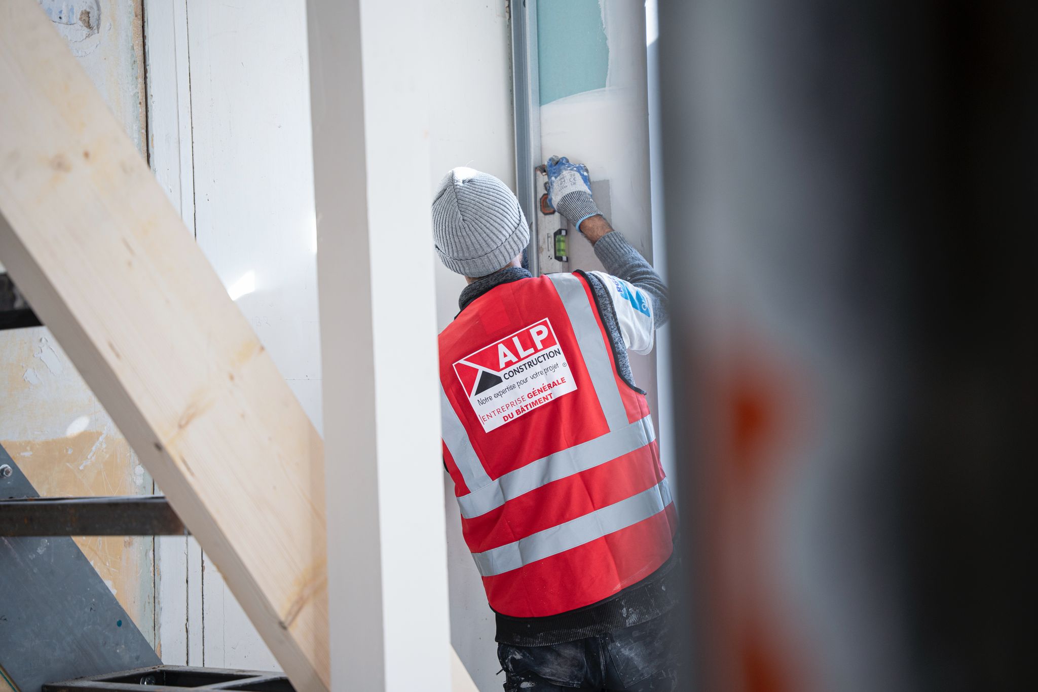Un salarié en gilet ALP intervient en hauteur sur un mur intérieur, à côté d’une ouverture.