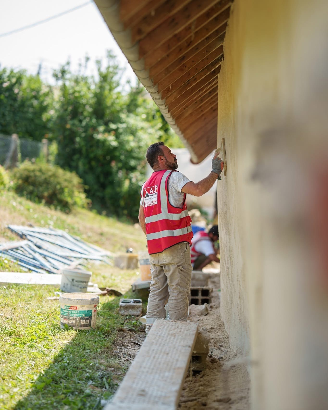 Un façadier ALP taloche un mur extérieur sous une avancée de toiture en bois.