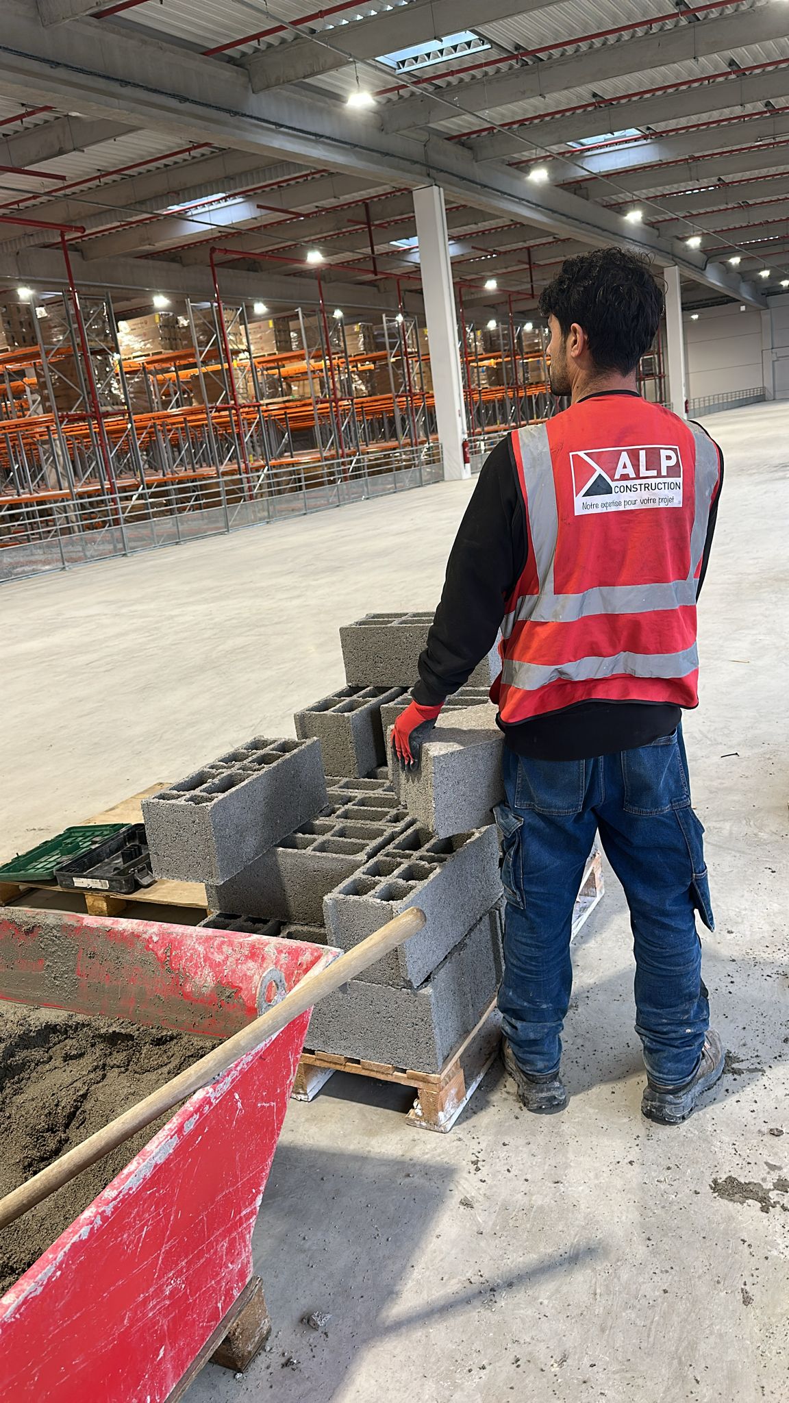 Un salari&eacute; ALP apporte un parpaing sur une zone de ma&ccedil;onnerie, &agrave; c&ocirc;t&eacute; d&rsquo;une dalle r&eacute;cemment r&eacute;alis&eacute;e.