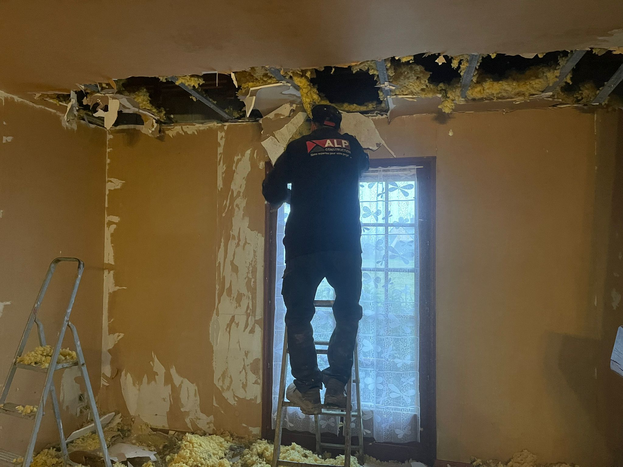 Un salari&eacute; ALP retire des &eacute;l&eacute;ments de plafond et d&rsquo;isolation depuis un escabeau.