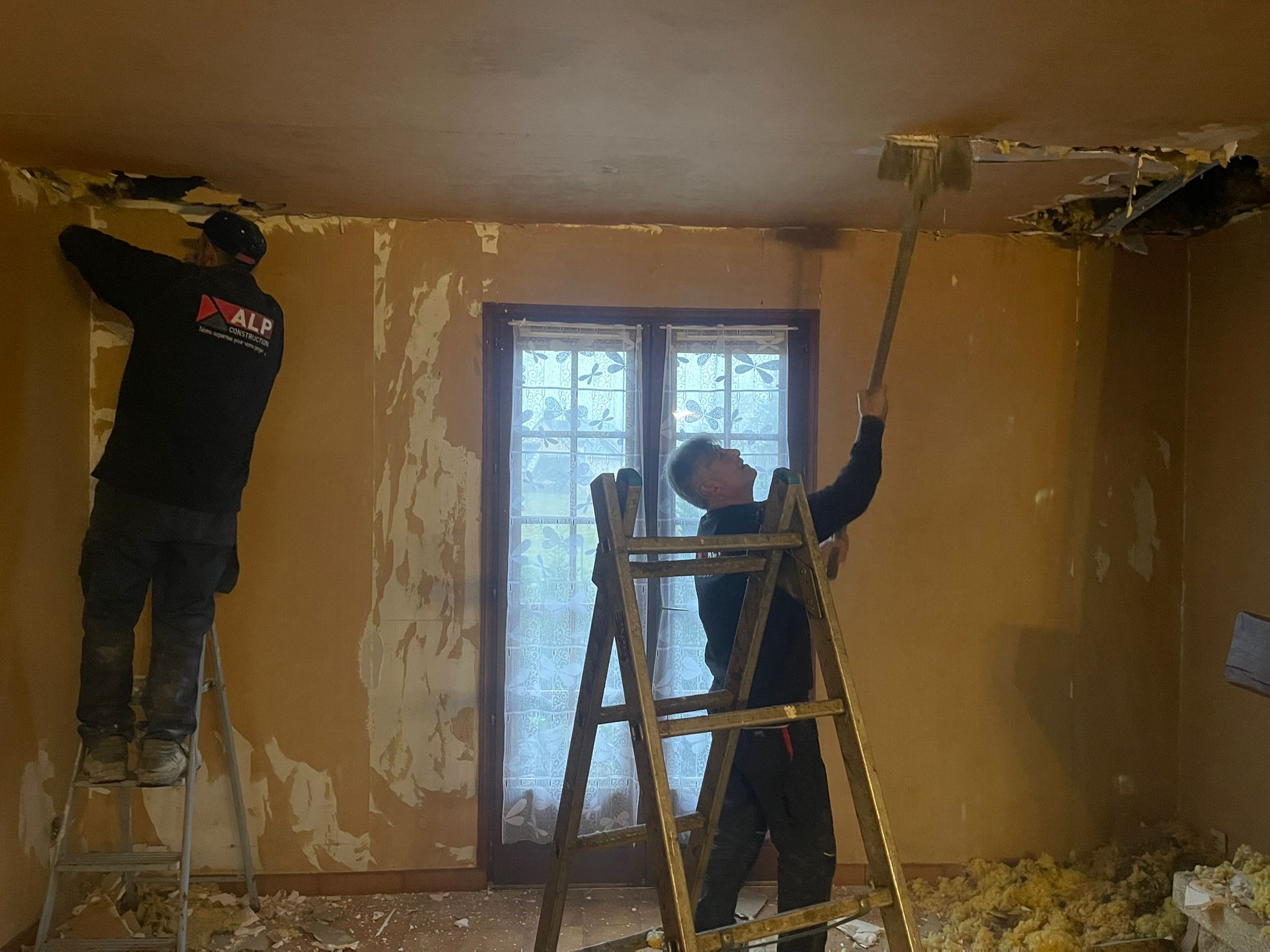 Deux salariés ALP travaillent en hauteur à la dépose d’un plafond dans une pièce en rénovation.